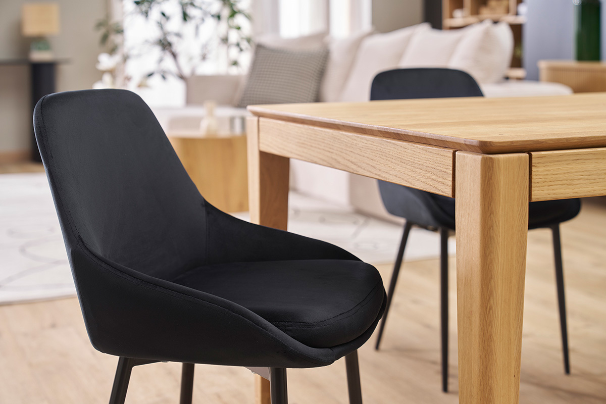 Chaise design noire en velours et m�tal vue lat�rale proche d'une table en bois.