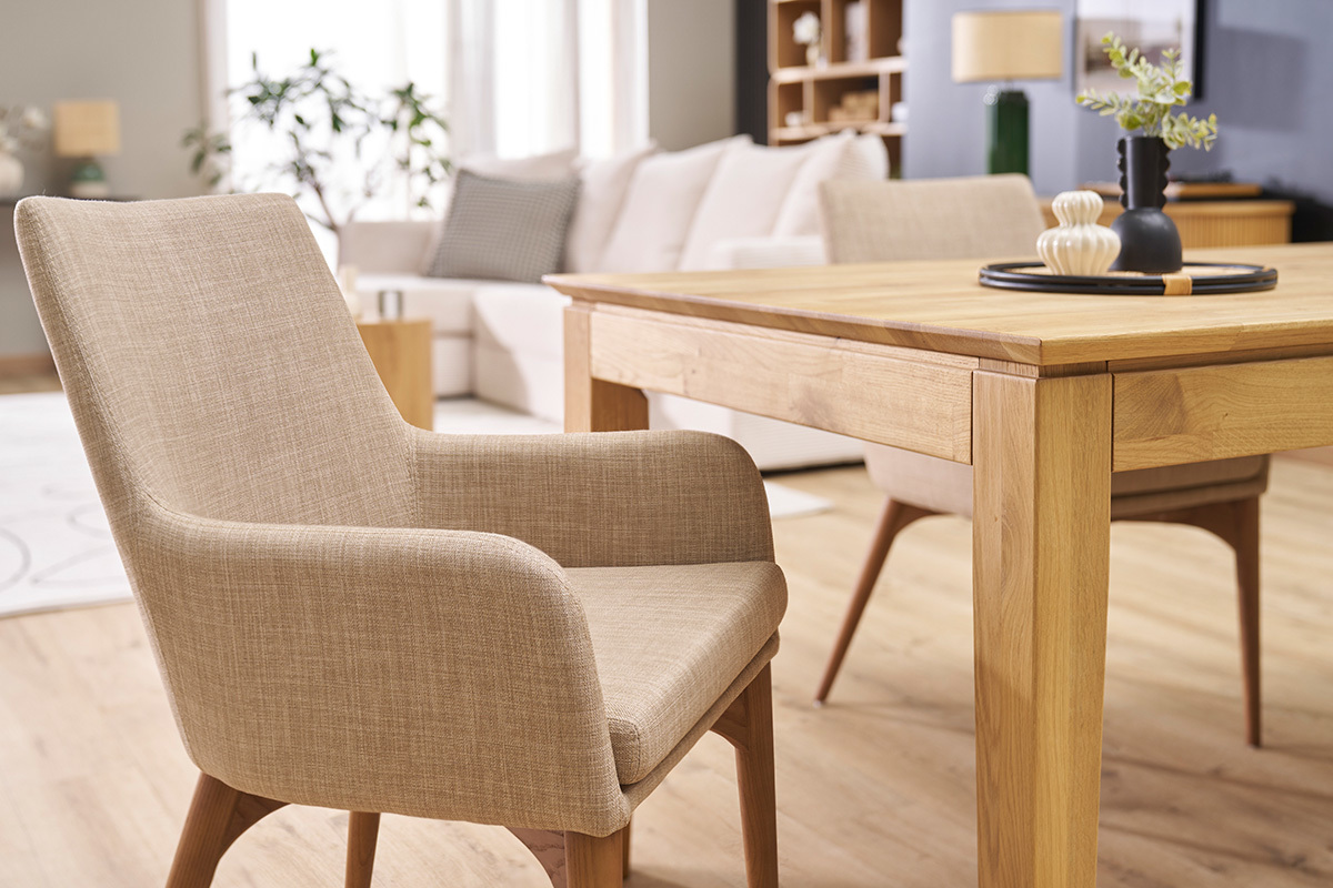 Chaise en tissu beige avec accoudoirs autour d'une table en bois, vue d'angle dans un int�rieur.