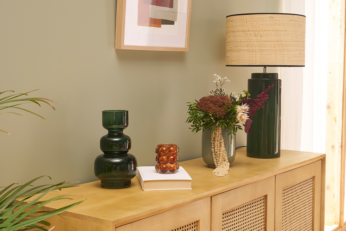 Lampe en c�ramique verte avec abat-jour raphia sur buffet, accompagn�e de vases d�coratifs.
