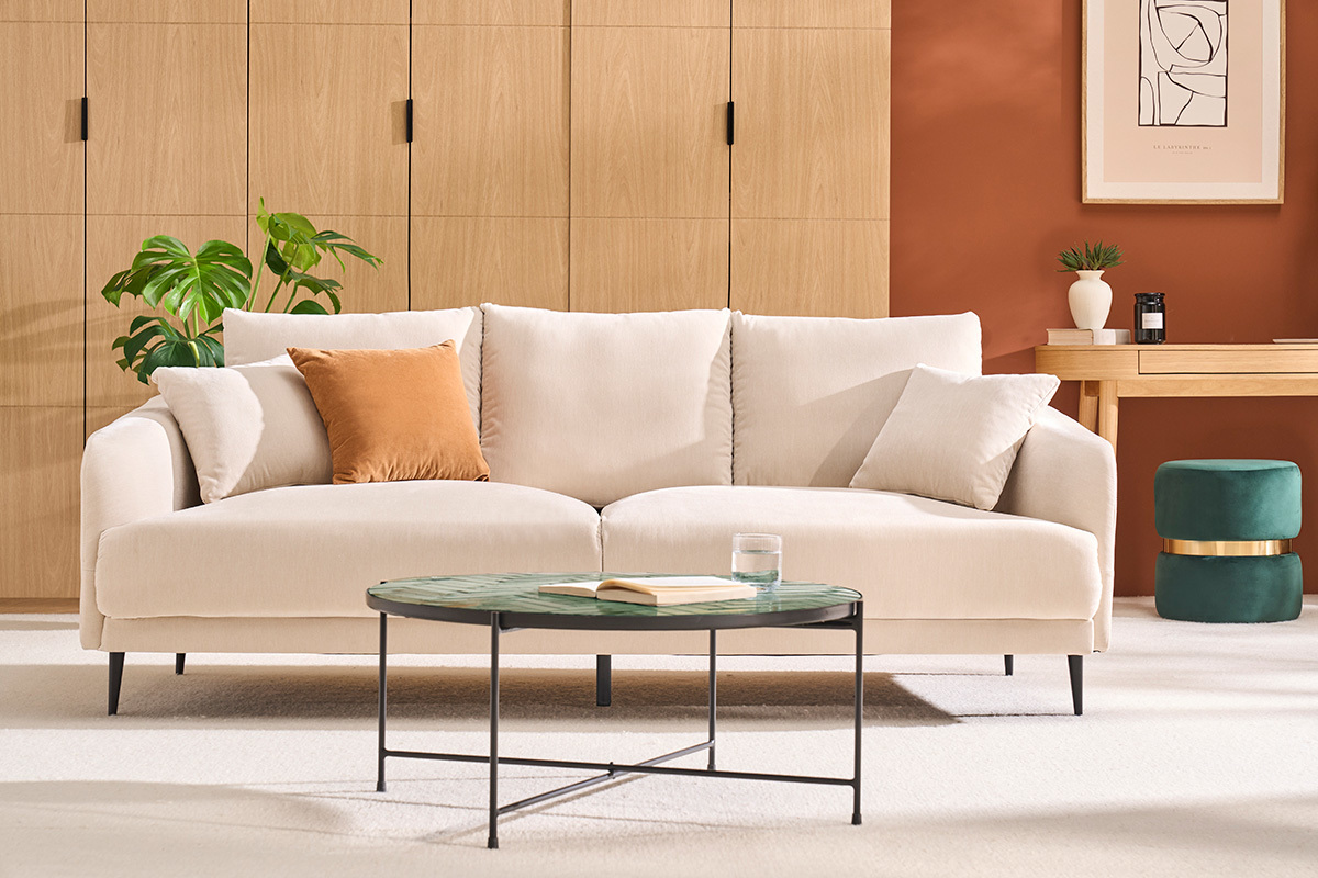 Pouf vert en velours avec bande dor�e derri�re un canap� dans un salon moderne.